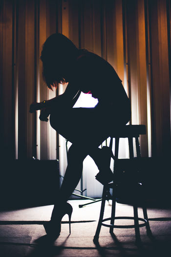 Silhouette woman sitting on chair at illuminated stage