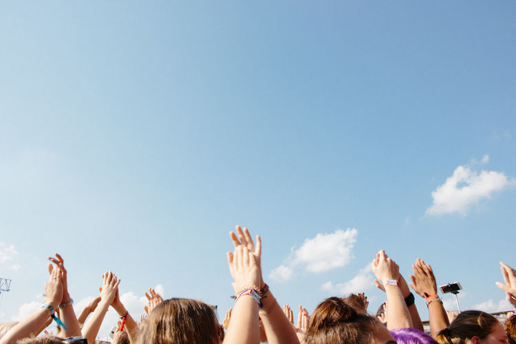 Crowd with arms raised against blue sky