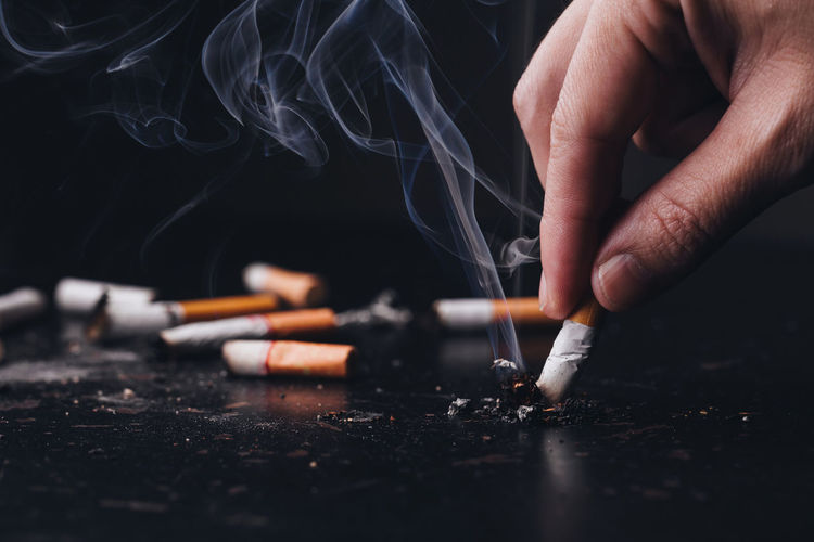 Cropped hand of person putting out cigarette against black background
