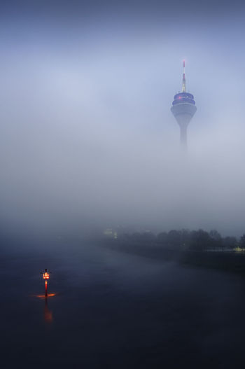 Communications tower by sea during foggy weather against sky