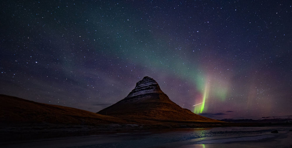 Scenic view of sea by mountain against sky at night