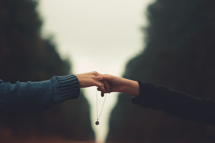 Cropped image of couple with necklace holding hands against sky