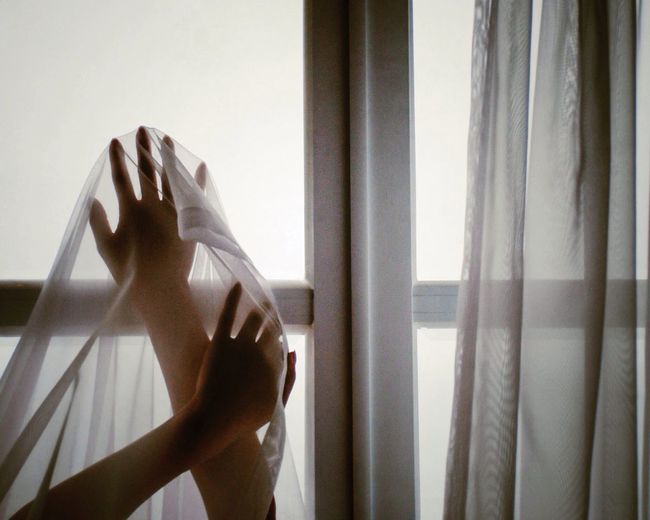 Close-up of hands holding curtain at window