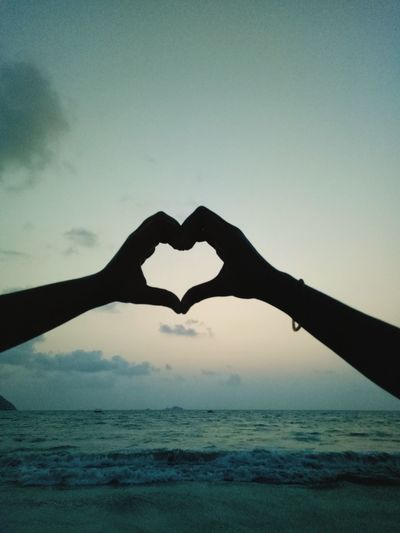 Close-up of hand holding heart shape over sea against sky