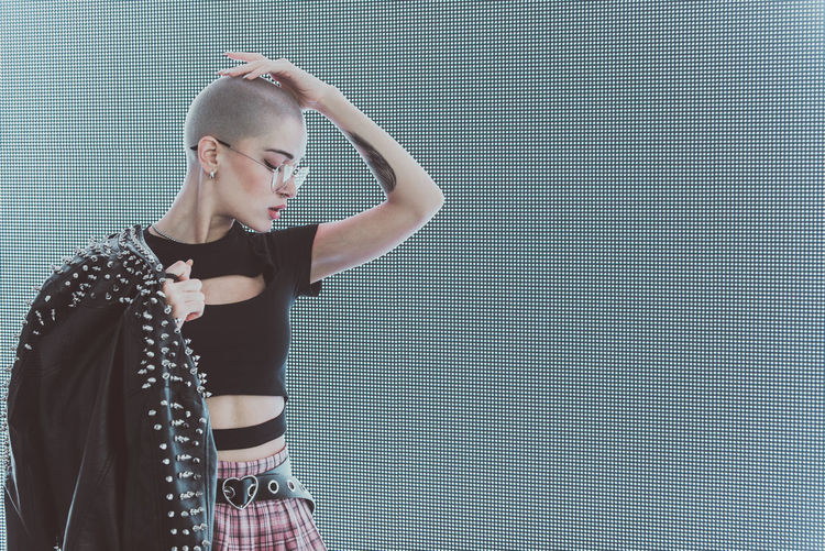 Young woman with shaved head standing against abstract backgrounds
