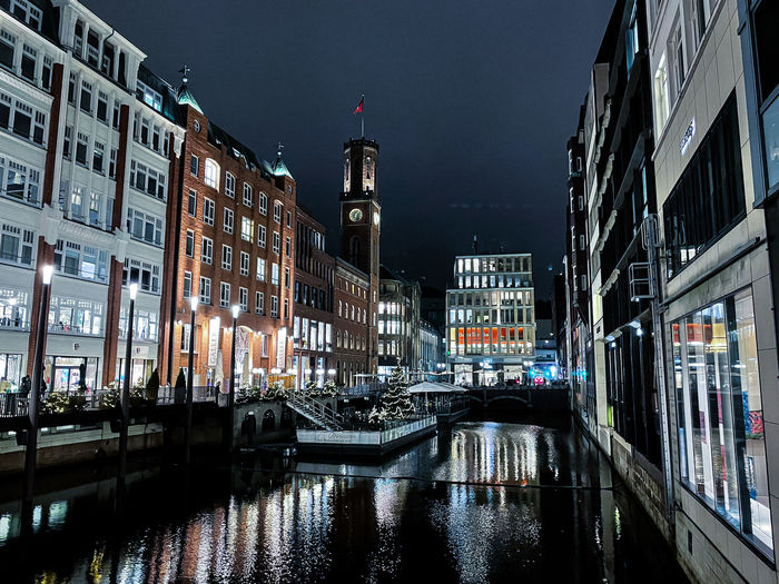 Canal by illuminated buildings in city at night