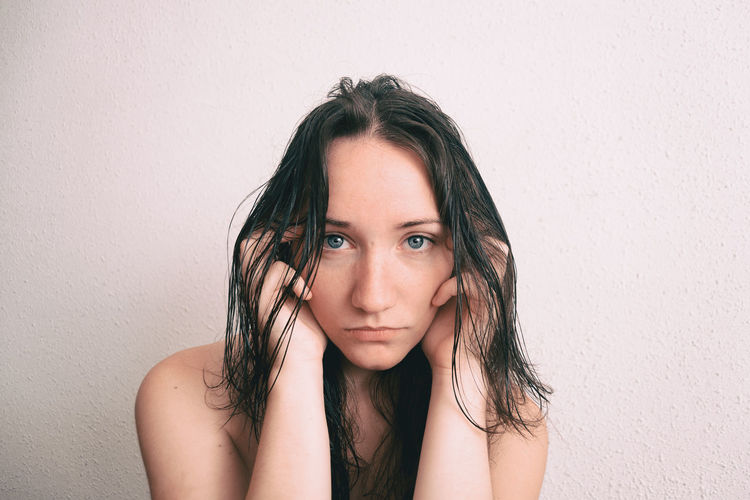 Portrait of young woman with messy hair against wall