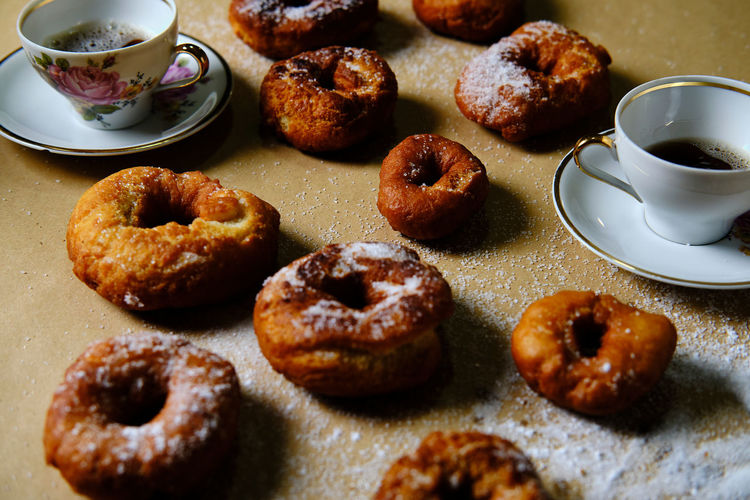 Top view of yummy doughnuts with powdered sugar and cups of hot tea placed on table at home