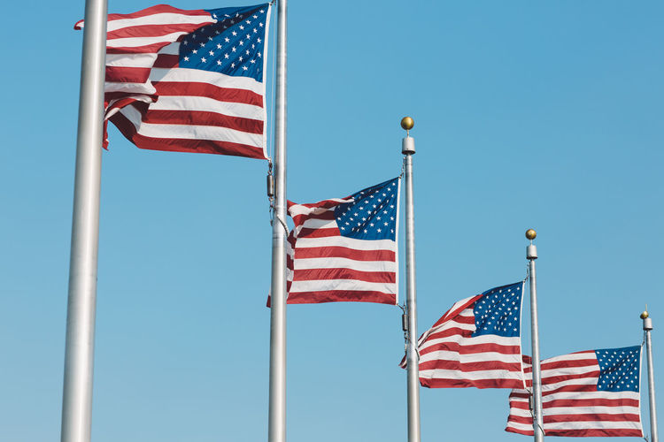 Low angle view of american flags fluttering against clear blue sky