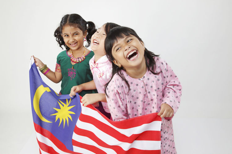 Cheerful girls holding malaysian flag while standing against white background