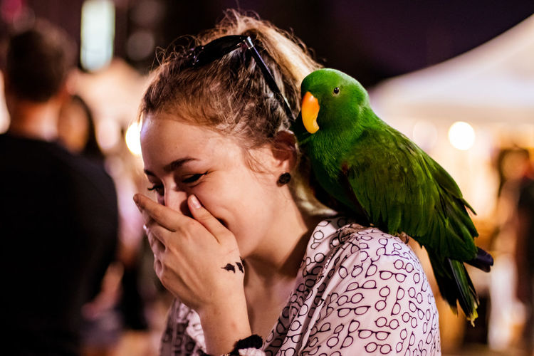 Close-up of happy woman with parrot on shoulder at night