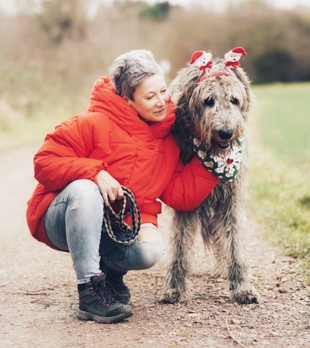 Mature woman with dog crouching on field at park during winter