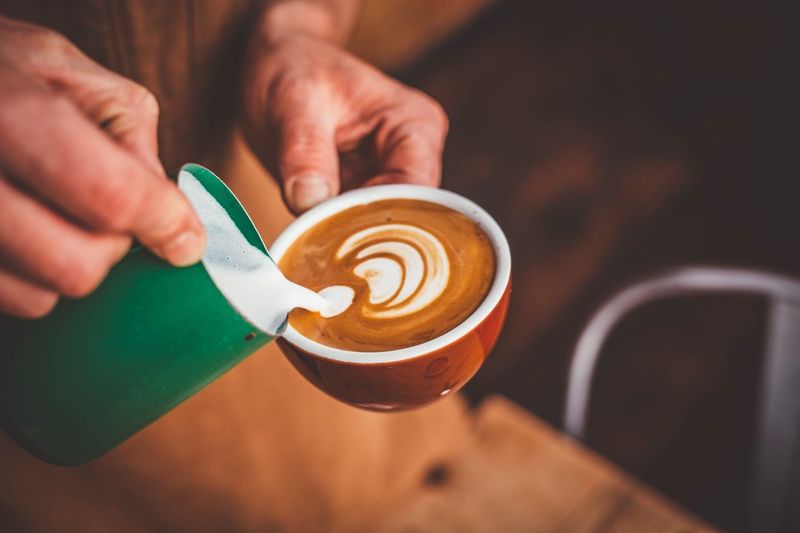 Cropped image of hand pouring milk into coffee cup