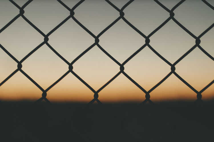 Silhouette chainlink fence against sky during sunset