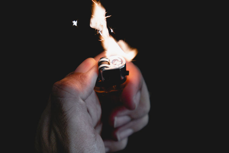 Close-up of hand holding cigarette lighter against black background