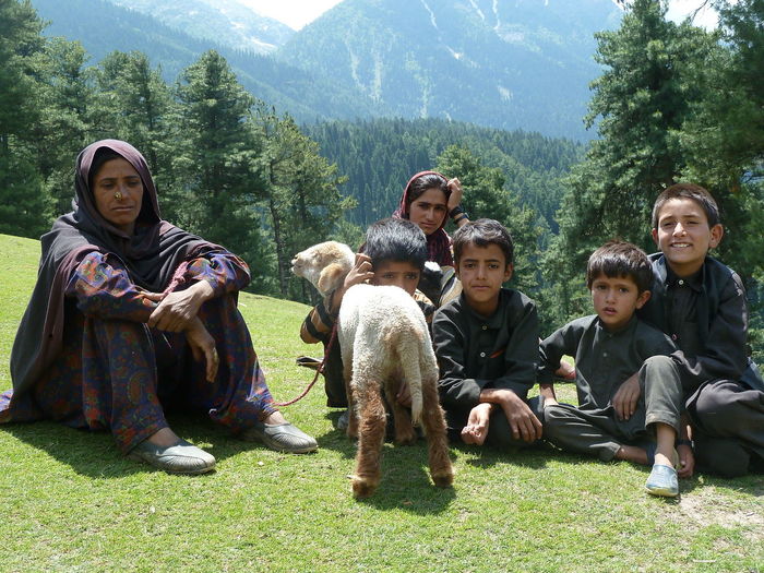 Family with sheep sitting on field against mountains