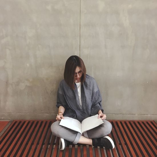 Woman reading book while sitting against wall
