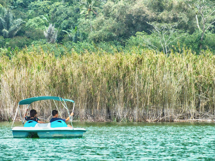Rear view of men sitting on boat in lake against trees