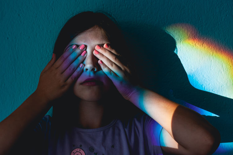 Close-up portrait of girl covering face against blue wall