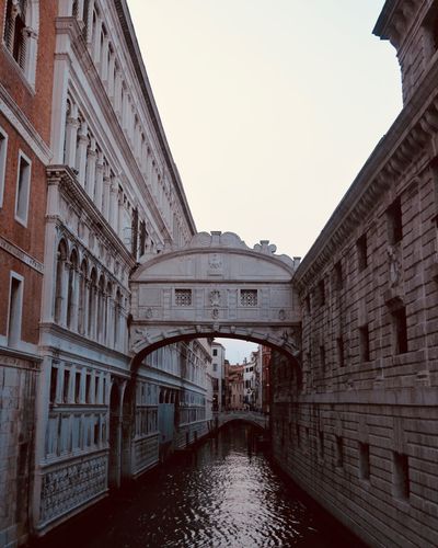 Arch bridge over canal amidst buildings against sky in city