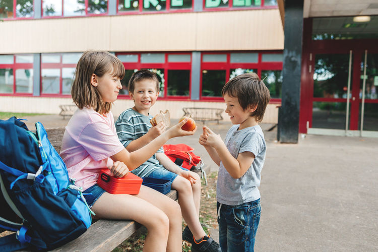 Children sit on a bench in the school yard and eat apples and sandwiches. snack during break 