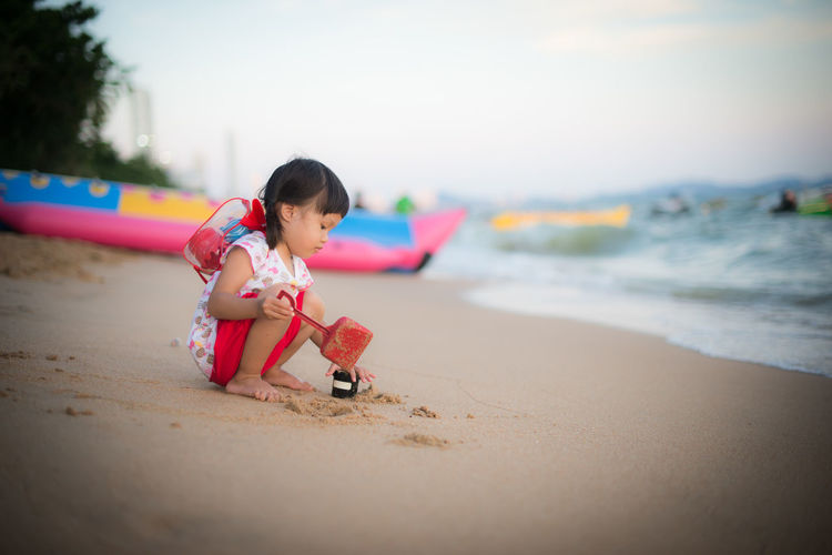 Girl playing on sand at beach against sky