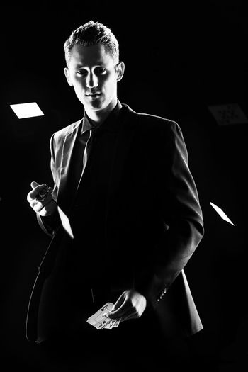 Portrait of man holding gambling chips and cards while standing against black background