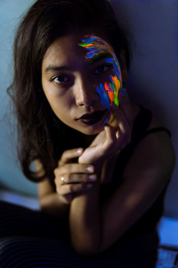 High angle portrait of young woman with face paint sitting in darkroom