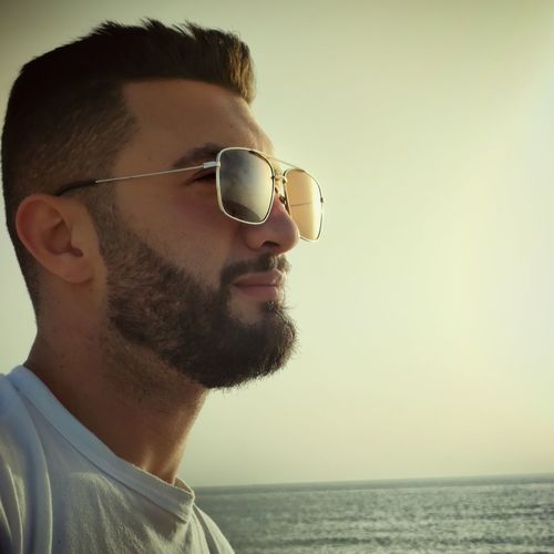 Portrait of young man wearing sunglasses against sea during sunset
