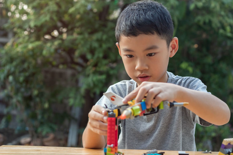 Short hair asian boy age 7 year old playing plastic toy blocks in his outdoor home garden