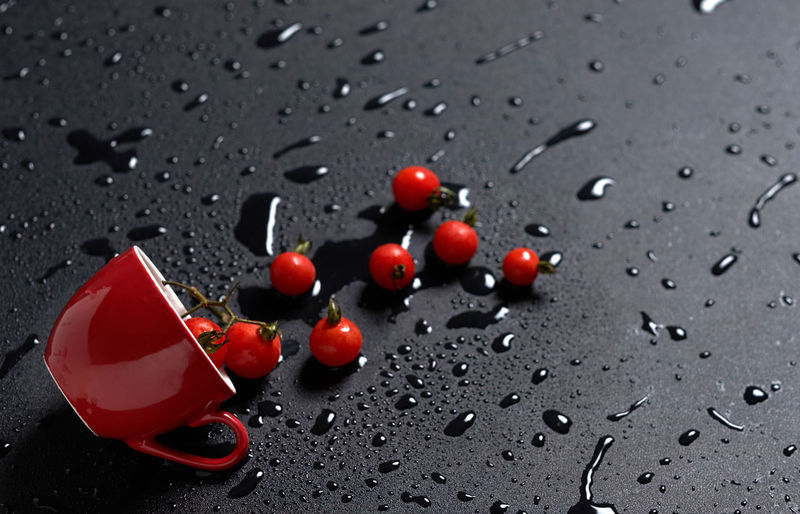 High angle view of fresh cherry tomatoes and red cup on wet table