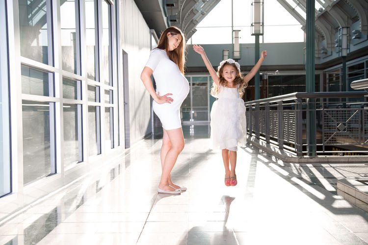 Portrait of happy daughter jumping by pregnant mother at corridor