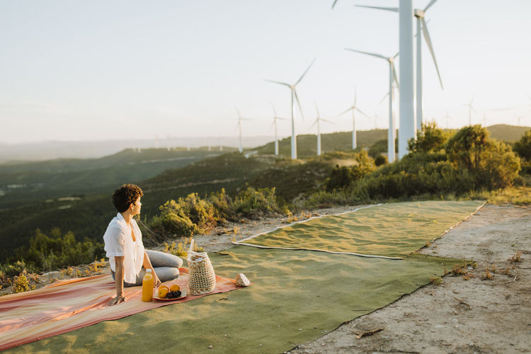 Woman looking at wind turbines while sitting on picnic blanket