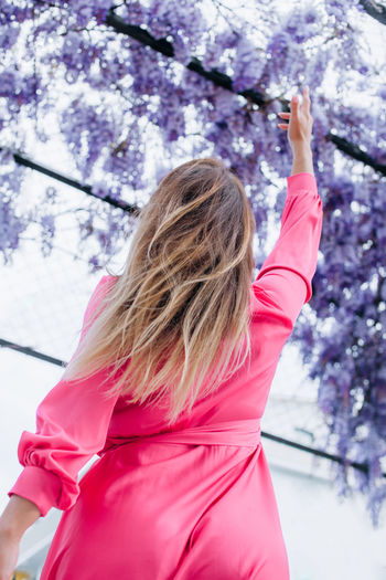 Pretty young woman is standing next to wisteria. girl enjoying spring time. spring outfit.