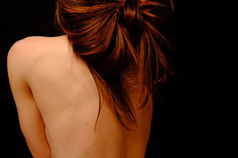 Rear view of seductive shirtless woman with brown hair over black background