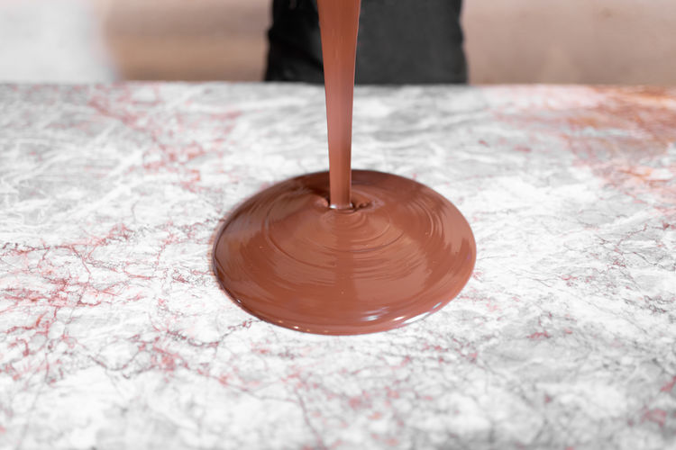 Chocolate liquid pouring on marble board during work in confectionery