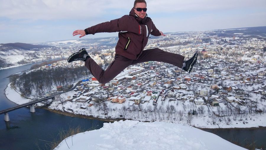 Full length of man jumping on snow against cityscape and sky
