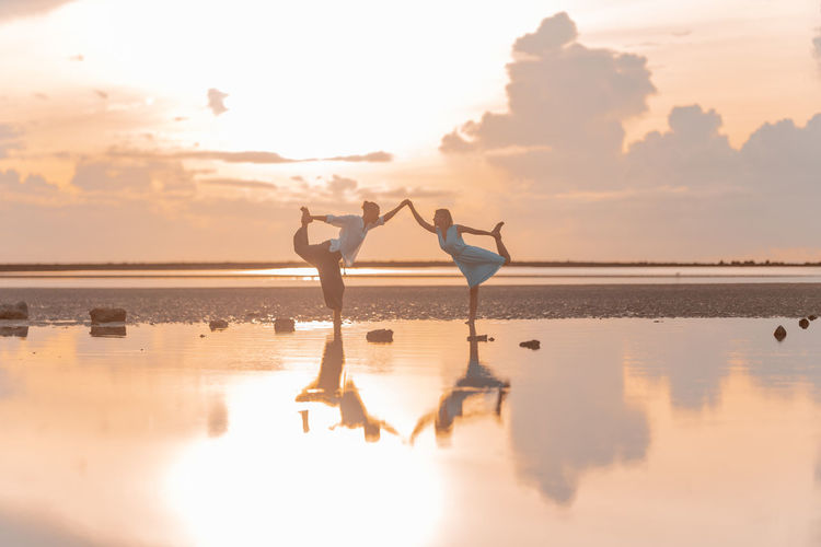 Man and woman doing yoga against the backdrop of the sunrise