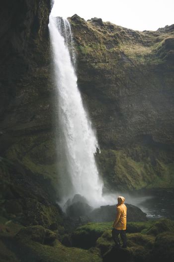 Man standing on cliff against waterfall