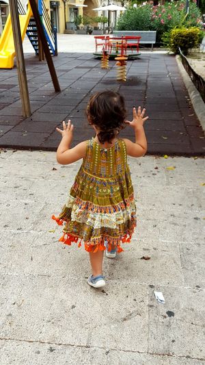Rear view of girl with arms raised on footpath