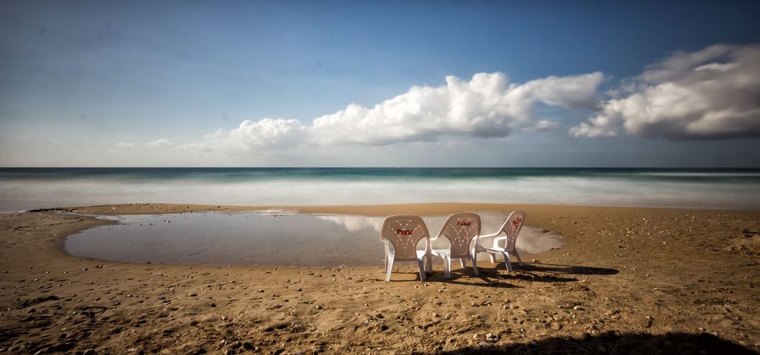 Chairs on sand at beach against sky