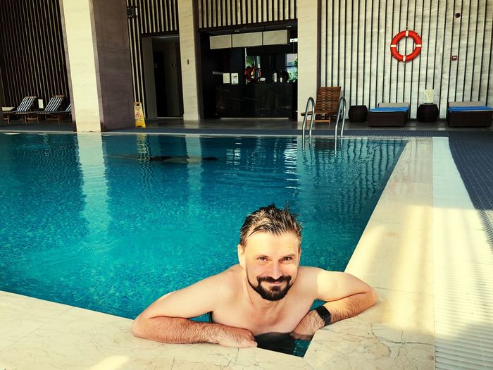 Portrait of smiling shirtless man swimming in pool