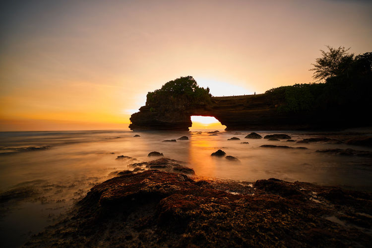 Scenic view of rock formation in sea against sky during sunset