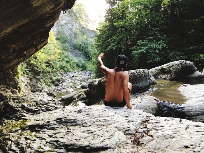 Rear view of shirtless man on rock in forest