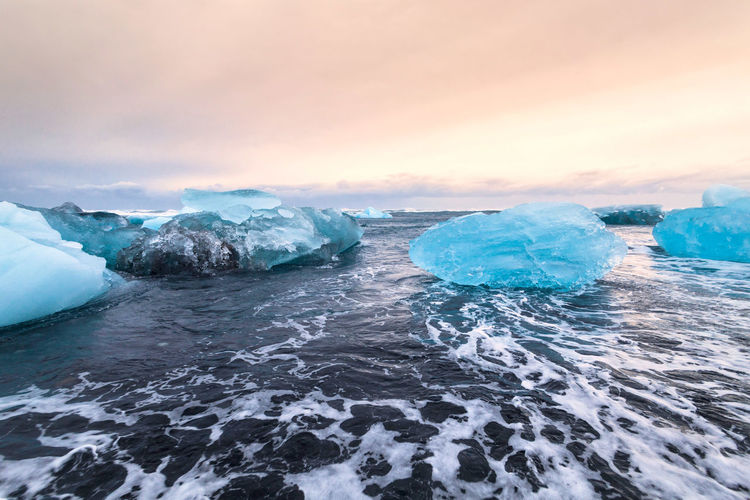 Scenic view of ice bergs floating on sea against cloudy sky during sunset
