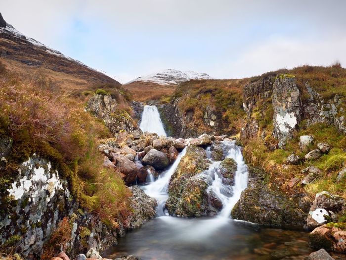 Rapids in small waterfall on stream, higland in scotland an early spring day. snowy cone of mountain
