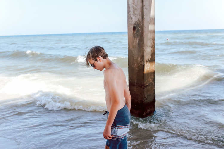 Full length of shirtless man standing at beach against sky