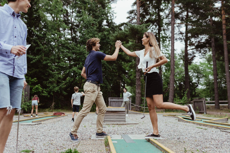Full length of friends giving high-five while playing miniature golf in backyard