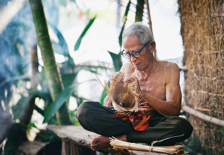 Senior man making craft product while sitting outdoors