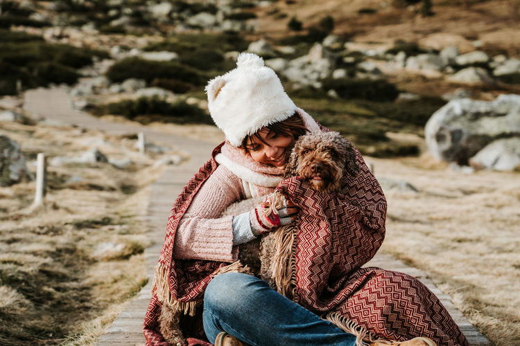 Woman wearing knit hat sitting in footpath with dog against field